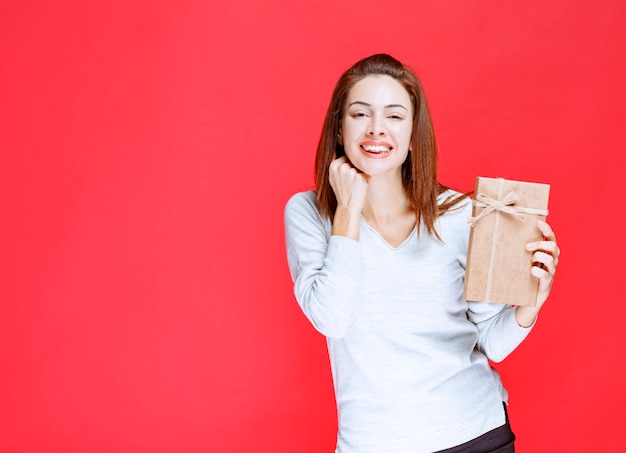 Jeune femme en chemise blanche tenant une boîte-cadeau en carton et a l'air surpris