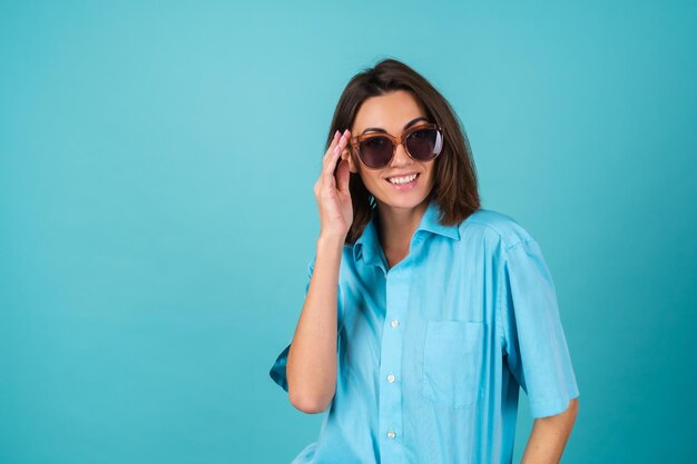 Jeune femme en chemise bleue sur un mur en lunettes de soleil, posant à la mode