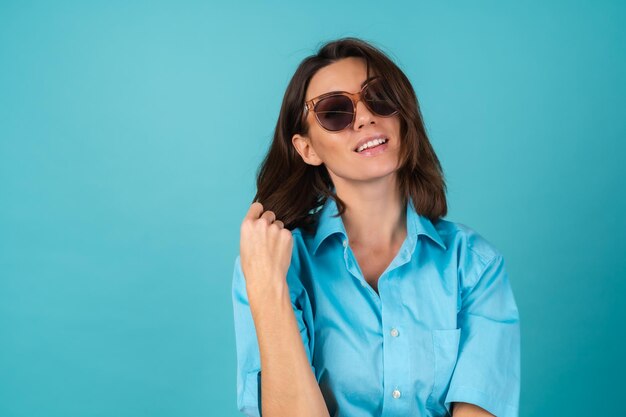 Jeune femme en chemise bleue sur un mur en lunettes de soleil, posant à la mode