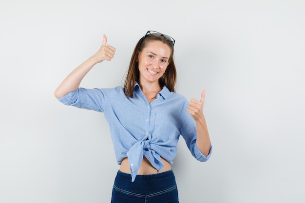 Jeune femme en chemise bleue, pantalon montrant les pouces vers le haut et à la satisfaction