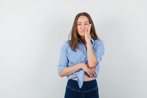 Jeune femme en chemise bleue, pantalon tenant la paume sur la joue et à la fatigue