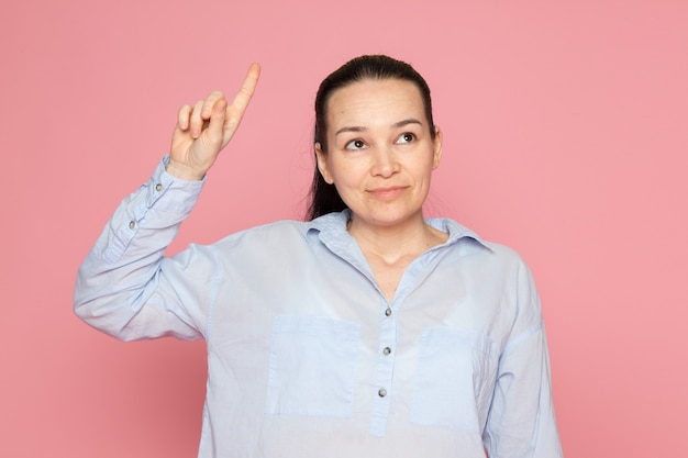 jeune femme en chemise bleue posant sur le mur rose