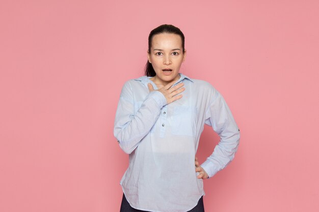 jeune femme en chemise bleue posant sur le mur rose