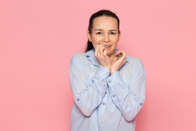 jeune femme en chemise bleue posant sur le mur rose