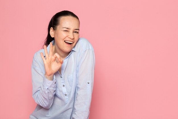 jeune femme en chemise bleue posant sur le mur rose