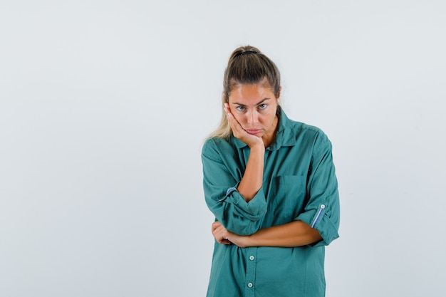 Jeune femme en chemise bleue regardant la caméra tout en se penchant sur son coude et à l'ennui