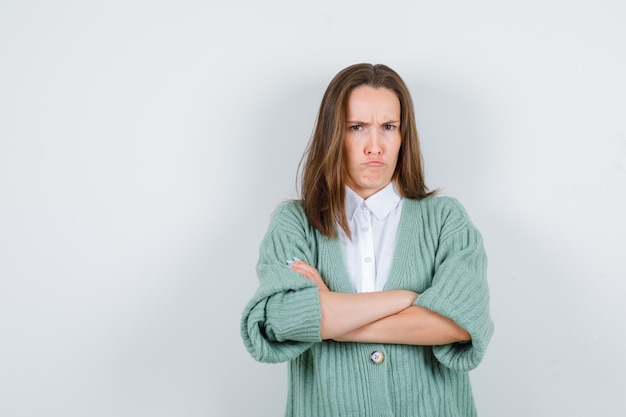 Jeune femme en chemise, cardigan debout avec les bras croisés et à la recherche de ressentiment, vue de face.