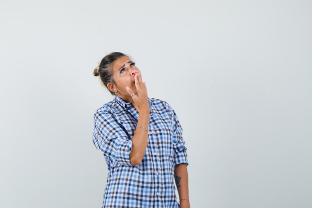 Jeune femme en chemise à carreaux bâillant avec la main sur la bouche.