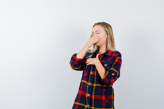 Jeune femme en chemise à carreaux bâillements et à la vue de face, somnolent.