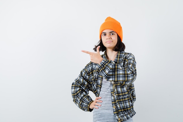 Jeune femme en chemise à carreaux chapeau orange pointant vers le côté à heureux