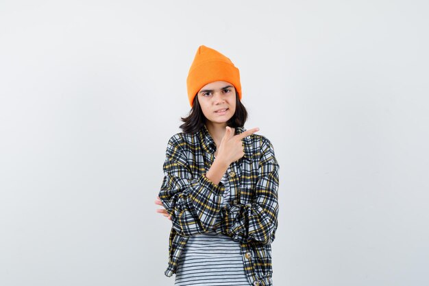 Jeune femme en chemise à carreaux chapeau orange pointant vers le côté à l'incertitude