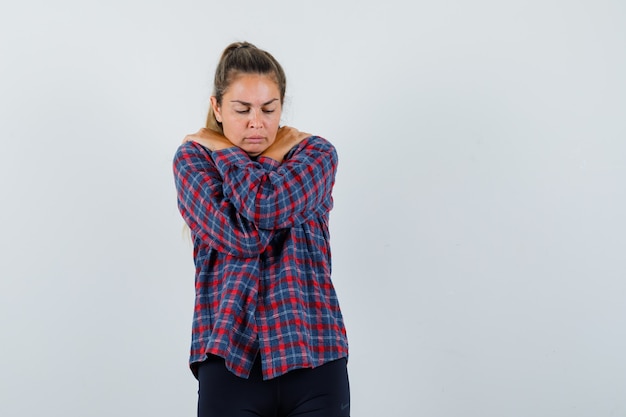 Jeune femme en chemise à carreaux debout les bras croisés, frissonnant de froid et à la fatigue