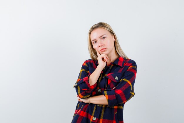 Jeune femme en chemise à carreaux debout dans la pensée pose et à la vue de face, confiant.