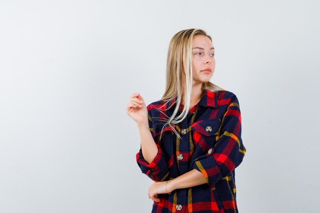 Jeune femme en chemise à carreaux en détournant les yeux tout en posant et en regardant attrayante, vue de face.