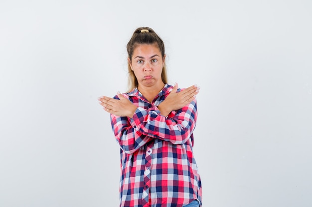 Jeune femme en chemise à carreaux gardant les bras croisés sur la poitrine et regardant confus, vue de face.