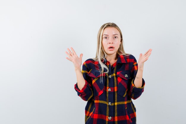 Jeune Femme En Chemise à Carreaux Gardant Les Mains De Manière Agressive Et à La Perplexité, Vue De Face.