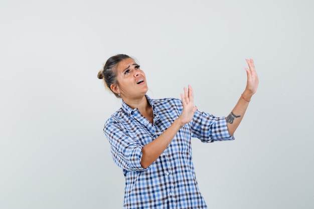 Jeune femme en chemise à carreaux levant les mains pour se défendre et à la peur.