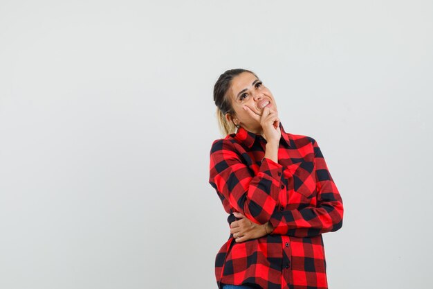 Jeune femme en chemise à carreaux en levant et à la rêveuse, vue de face.