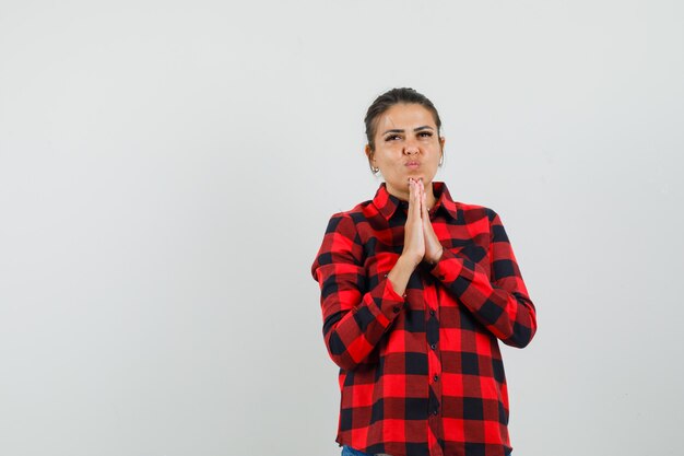 Jeune femme en chemise à carreaux main dans la main en signe de prière et à la recherche d'espoir, vue de face.