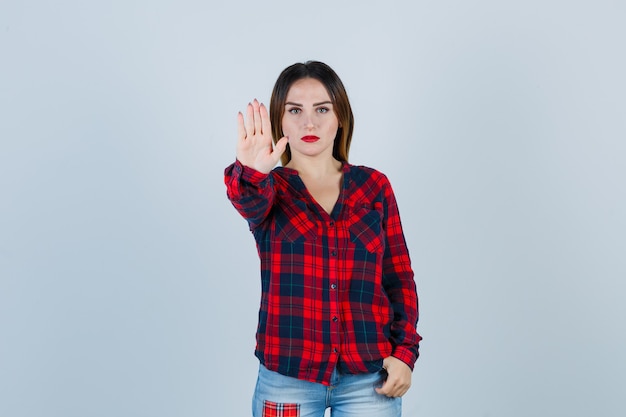 Jeune femme en chemise à carreaux montrant un geste d'arrêt et semblant résolue, vue de face.