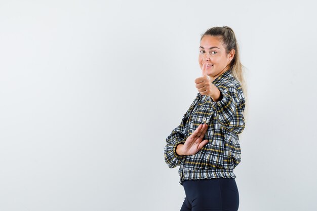 Jeune femme en chemise à carreaux montrant le pouce vers le haut et l'air confiant.