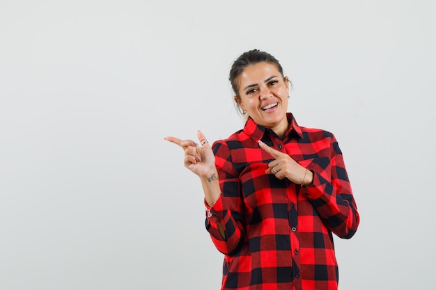 Jeune femme en chemise à carreaux pointant sur le côté et à la joyeuse