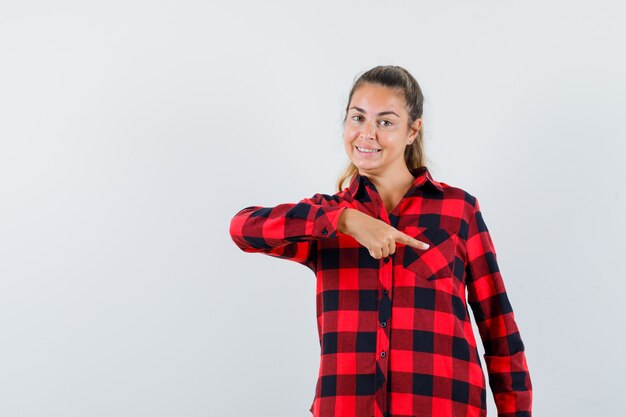 Jeune femme en chemise à carreaux pointant vers le bas et à la joyeuse