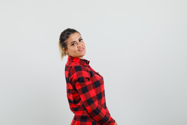 Jeune femme en chemise à carreaux regardant la caméra par-dessus son épaule et à la belle.