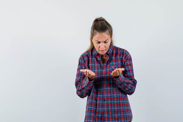 Jeune femme en chemise à carreaux regardant les paumes comme tenant quelque chose et à la recherche concentrée