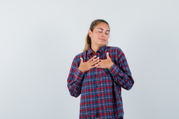 Photo gratuite jeune femme en chemise à carreaux reposant les mains sur la poitrine et à la calme
