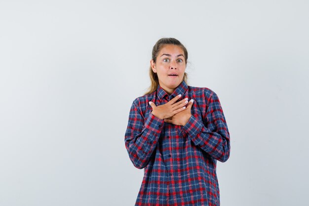 Jeune femme en chemise à carreaux reposant les mains sur la poitrine et à la surprise