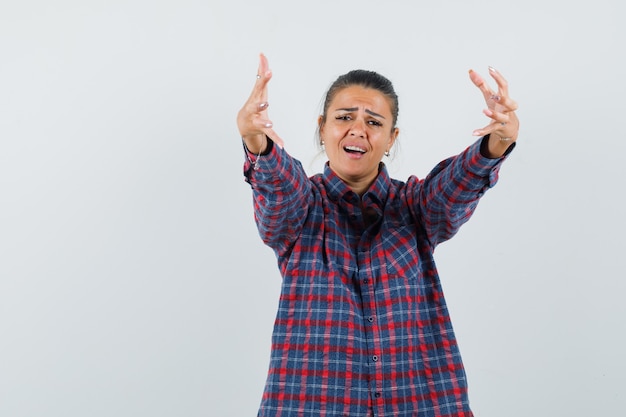 Jeune femme en chemise à carreaux s'étendant les mains comme tenant quelque chose et à la vue fatiguée, de face.