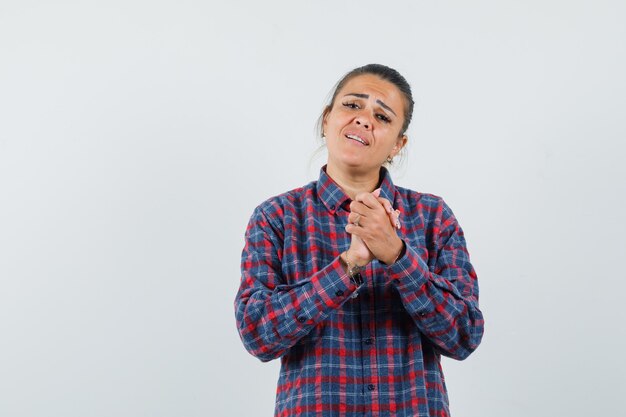 Jeune femme en chemise à carreaux se frottant les mains et à la vue de face, épuisée.