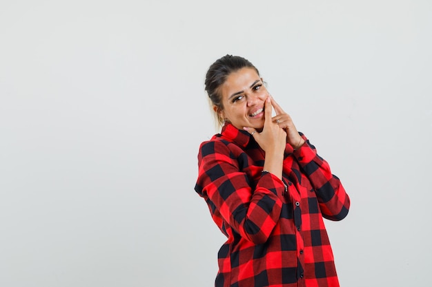 Photo gratuite jeune femme en chemise à carreaux serrant son bouton sur la joue et à la joie