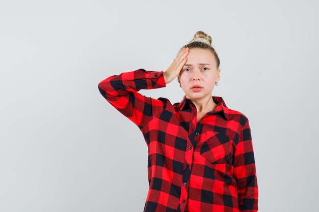 Jeune femme en chemise à carreaux tenant la main sur le front et à la détresse