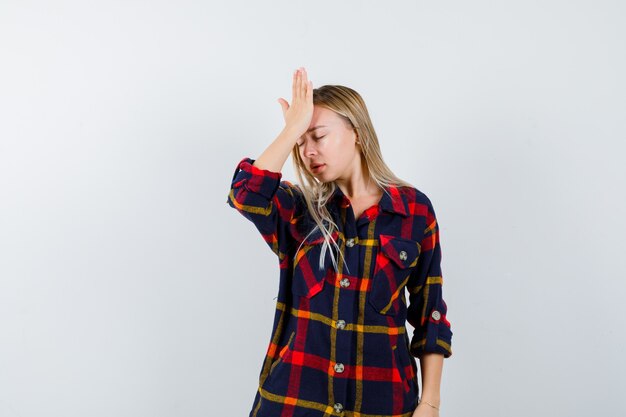 Jeune femme en chemise à carreaux tenant la main sur le front et à la vue de face, oublieux.