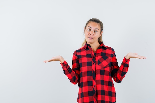 Jeune femme en chemise décontractée faisant le geste des échelles et regardant confiant, vue de face.