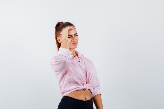 Jeune femme en chemise décontractée, pantalon tenant la main sur le front et à la vue épuisée, de face.