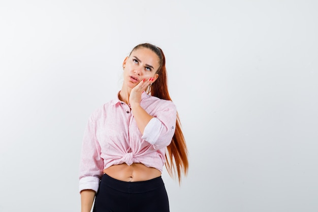 Jeune femme en chemise décontractée tenant la main sur la joue et regardant réfléchie, vue de face.