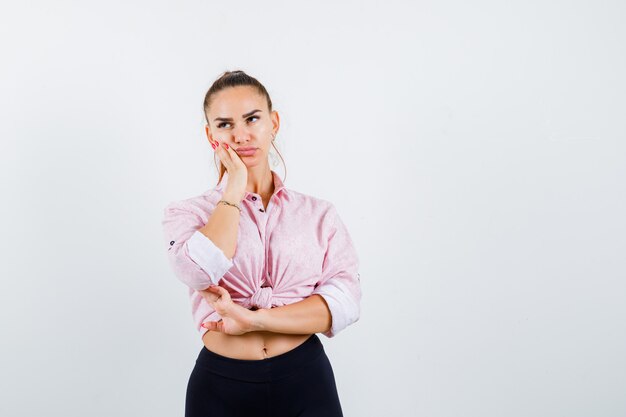 Jeune femme en chemise décontractée tenant la main sur la joue et regardant réfléchie, vue de face.