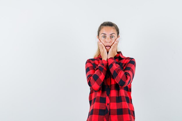 Jeune femme en chemise décontractée tenant les mains sur les joues et à la vue anxieuse, de face