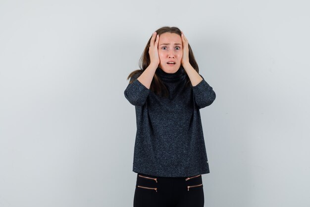 Jeune femme en chemise décontractée, tenant les mains sur la tête et à la nostalgie