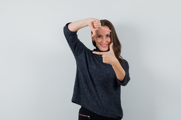 Jeune femme en chemise faisant le geste du cadre et à la joyeuse