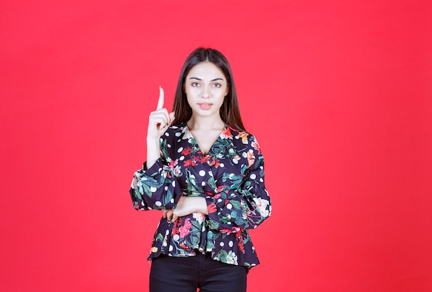 Jeune femme en chemise à fleurs debout sur un mur rouge et montrant à l'envers