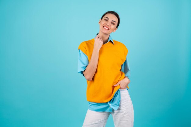 Jeune femme en chemise et gilet orange sur fond turquoise sourit joyeusement, regarde la caméra