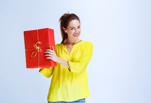 Jeune femme en chemise jaune tenant une boîte-cadeau rouge donnée à la Saint-Valentin