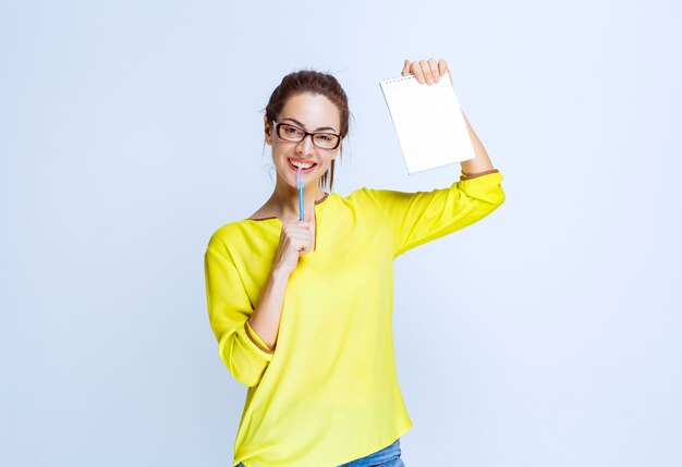 Jeune femme en chemise jaune tenant sa feuille d'examen et pensant tout en tenant un stylo