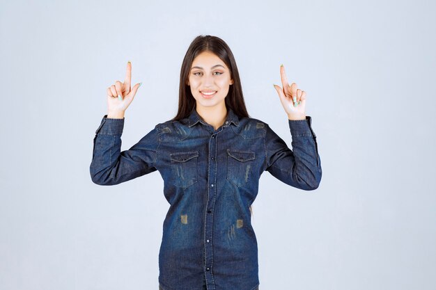 Jeune femme en chemise en jean levant les mains et montrant quelque chose au-dessus