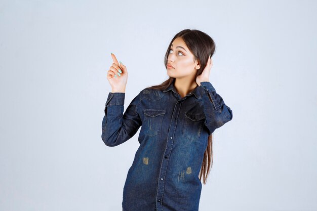 Jeune femme en chemise en jean levant les mains et montrant quelque chose au-dessus