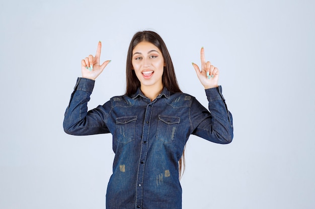 Jeune femme en chemise en jean montrant quelque chose à l'envers